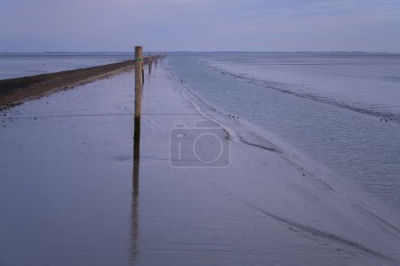 Navigable channel leading away from the harbor in Neuharlingersiel at low tide with the wadden sea ocean floor revealed around it. The island of Spiekeroog Germany is visible in the distance.
