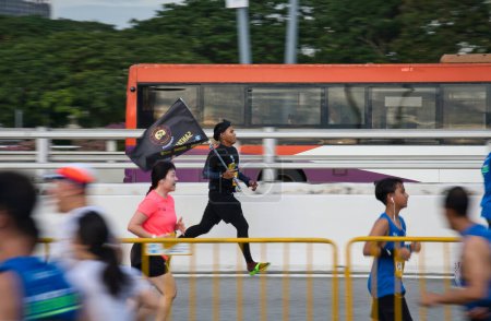 Téléchargez les photos : Singapour - 2 déc. 2023 : Coureur en pantoufles portant un drapeau lors du Standard Chartered Singapore Marathon 2023. - en image libre de droit