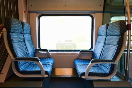 Téléchargez les photos : Sièges bleus vides dans le train de voyageurs, lumière du soleil éclatante à l'extérieur. - en image libre de droit
