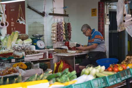 Téléchargez les photos : Singapour - 28 septembre 2022 : Gardien de magasin âgé dans un étal de produits frais du marché dans le bloc HDB 846 Yishun Ring Road, vendant des fruits et légumes. - en image libre de droit