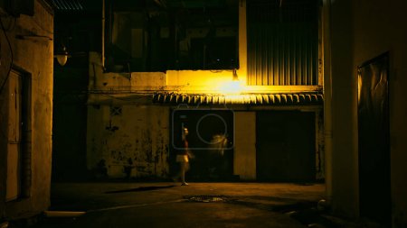 Téléchargez les photos : Personne marchant dans une ruelle sombre la nuit, éclairée par un lampadaire. Mouvement flou. - en image libre de droit