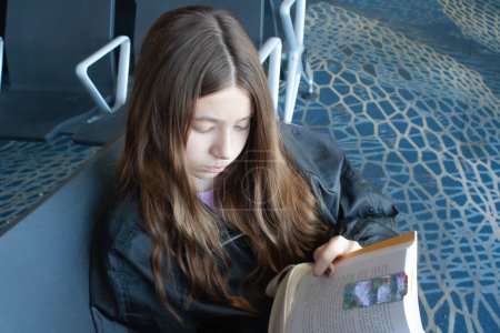 Teenager waits for the departure of her next plane reading a book
