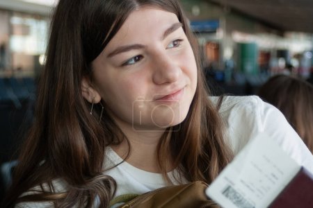 Junges Mädchen blickt mit ihren Reisedokumenten durch das Flughafenfenster