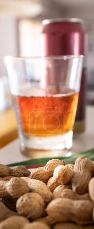 Verre rafraîchissant de bière rouge et une poignée d'arachides décortiquées sur une table mis hors foyer arrière-plan