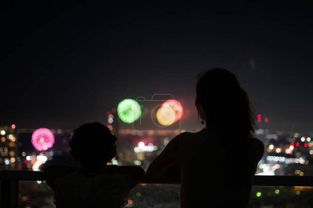 Foto de Madre e hija viendo fuegos artificiales desde el balcón - Imagen libre de derechos