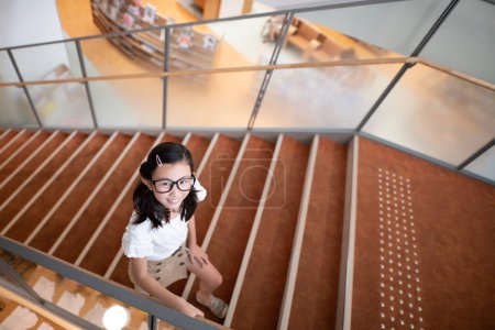 Téléchargez les photos : Fille monter les escaliers dans la bibliothèque - en image libre de droit