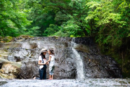 Photo for Mother and daughter enjoying view of a waterfall at the forest, in the morning - Royalty Free Image