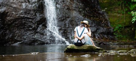 Téléchargez les photos : Mère et fille profitant d'une vue sur une cascade à la forêt, le matin - en image libre de droit