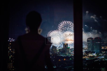 Foto de Mujer ver los fuegos artificiales desde la ventana del apartamento - Imagen libre de derechos