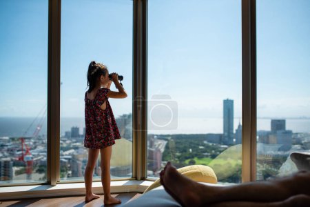 Photo for Girl watching the view with binoculars from the window of the apartment - Royalty Free Image