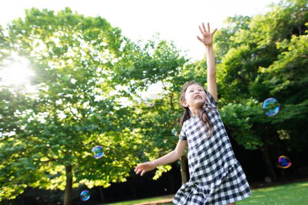Téléchargez les photos : Jeune asiatique fille jouer avec savon bulles dans parc - en image libre de droit