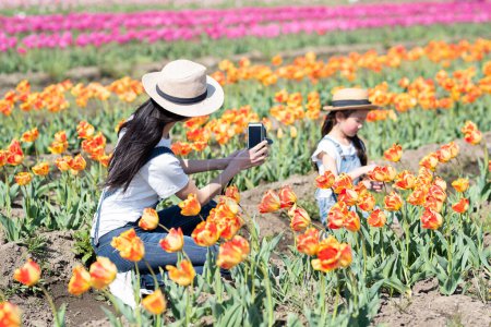 Téléchargez les photos : Mère et fille prenant des photos dans le champ de fleurs - en image libre de droit