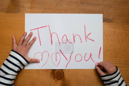 Téléchargez les photos : Un enfant écrit merci sur papier - en image libre de droit