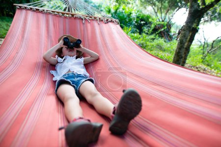 Téléchargez les photos : Fille qui utilise des jumelles couchées sur un hamac - en image libre de droit
