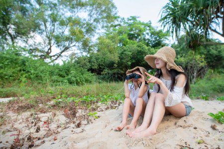 Photo for Young woman and girl  with binoculars sitting on beach - Royalty Free Image