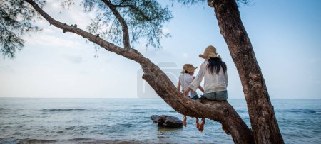 Téléchargez les photos : Mère et fille assises sur un arbre à la plage - en image libre de droit