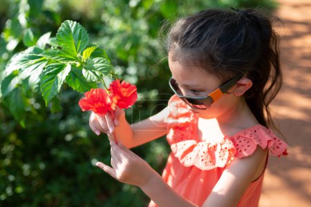 Téléchargez les photos : Fille regarder hibiscus fleur dans le jardin - en image libre de droit