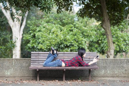 Téléchargez les photos : Femme pour utiliser le téléphone intelligent dans un banc de parc - en image libre de droit