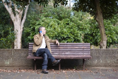 Téléchargez les photos : Homme pour utiliser le téléphone intelligent dans un banc de parc - en image libre de droit