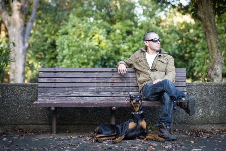 Foto de Hombre que se relaja con Doberman en el banco del parque - Imagen libre de derechos