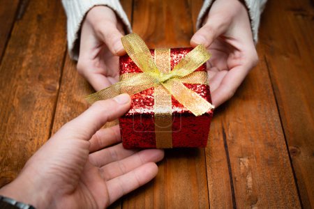 Téléchargez les photos : Mains de l'homme et de la femme tenant cadeau de Noël sur fond de table en bois - en image libre de droit