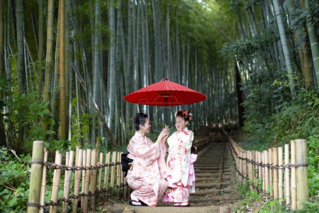 Téléchargez les photos : Jeune mère asiatique avec fille dans les robes japonaises traditionnelles dans la forêt de bambous - en image libre de droit