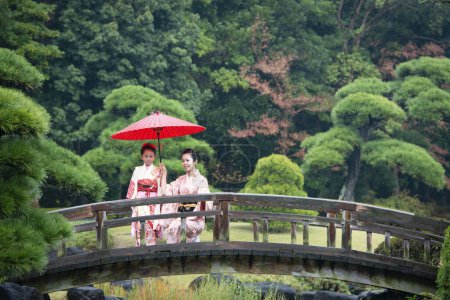 Téléchargez les photos : Jeune femme asiatique avec fille dans les robes japonaises traditionnelles dans le jardin avec parapluie dans le parc - en image libre de droit