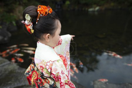 Téléchargez les photos : Belle fille en kimono près de l'étang avec des poissons koï - en image libre de droit