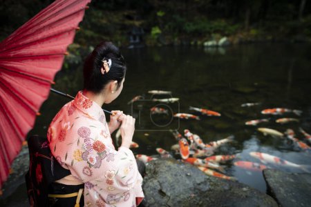 Téléchargez les photos : Fille avec parapluie en kimono près de l'étang avec des poissons koï - en image libre de droit