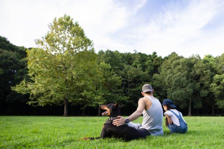 Téléchargez les photos : Père, fille et chien se relaxant dans le parc - en image libre de droit