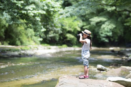 Téléchargez les photos : Enfant utilisant des jumelles au bord de la rivière - en image libre de droit