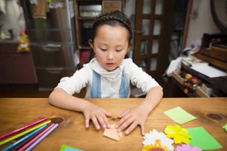Téléchargez les photos : Fille jouer avec origami à la table - en image libre de droit