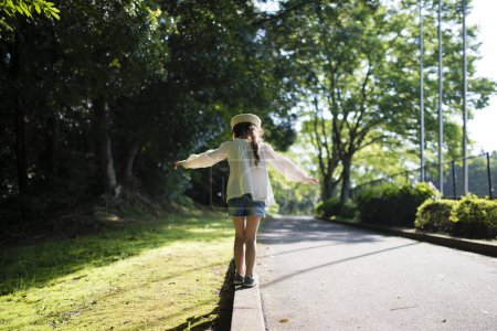 Photo for Little girl walking curb in sunny day - Royalty Free Image