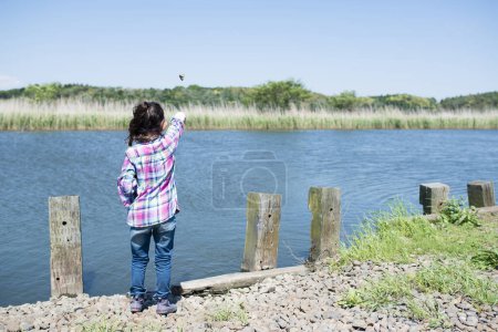Téléchargez les photos : Petite fille qui jette une pierre dans un étang - en image libre de droit