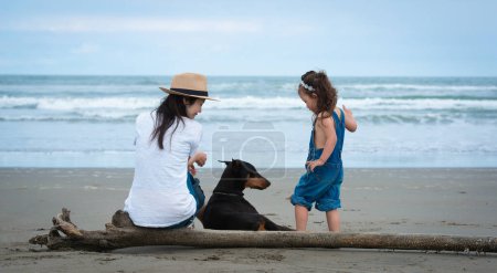Foto de Madre e hija y un perro sentado en la playa - Imagen libre de derechos