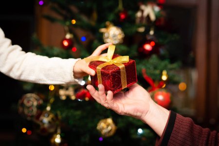 Téléchargez les photos : Mains de l'homme et la fille tenant cadeau de Noël sur fond de table en bois - en image libre de droit