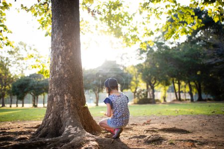 Photo for Girl playing squatting at the base of the tree - Royalty Free Image