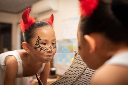 Téléchargez les photos : Petite fille asiatique portant costume pour halloween regarder dans le miroir - en image libre de droit