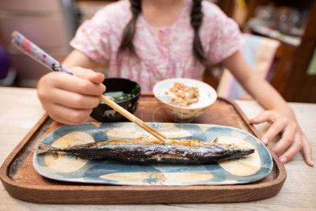 Foto de Asiático niña comer pescado con palillos en casa - Imagen libre de derechos