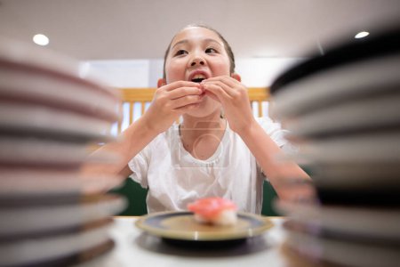 Foto de Niño comiendo sushi en la cinta transportadora sushi - Imagen libre de derechos