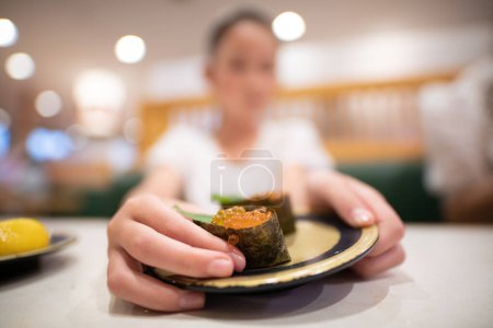 Téléchargez les photos : Un enfant qui mange des sushis aux oeufs de saumon - en image libre de droit