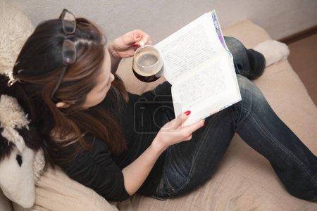 Téléchargez les photos : Femme lisant un livre tout en buvant du café - en image libre de droit