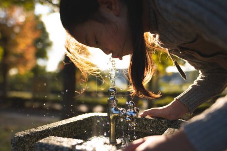 Photo for Girl drinking water at the water fountain in the park - Royalty Free Image