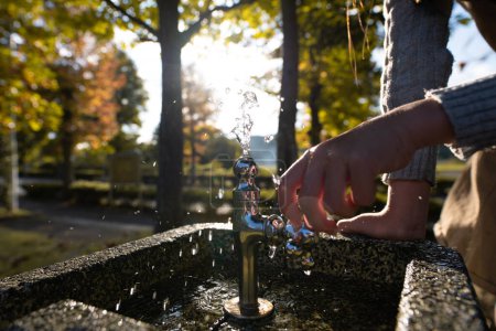 Téléchargez les photos : Main d'enfant touchant le robinet à la fontaine d'eau dans le parc - en image libre de droit