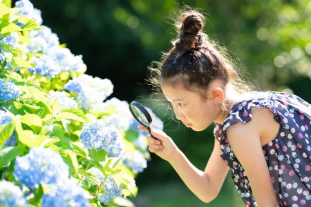 Foto de Retrato de niña mirando a través de lupa en flores - Imagen libre de derechos