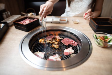 Téléchargez les photos : Une femme mange dans un restaurant japonais yakiniku - en image libre de droit