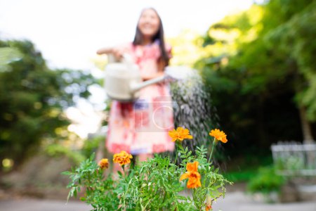 Téléchargez les photos : Une fille qui arrose des fleurs avec un arrosoir - en image libre de droit