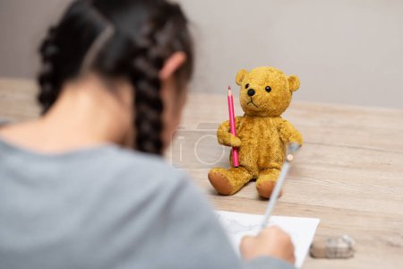 Téléchargez les photos : Un enfant étudie à la maison et un ours en peluche veille sur - en image libre de droit