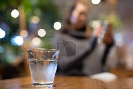 Téléchargez les photos : L'eau sur la table et la femme regardant smartphone derrière - en image libre de droit