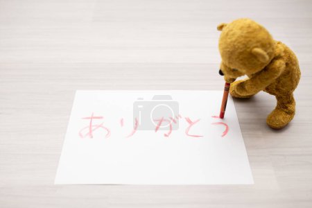 Foto de Osito de peluche escribiendo felicitaciones en japonés con lápices de colores sobre papel - Imagen libre de derechos